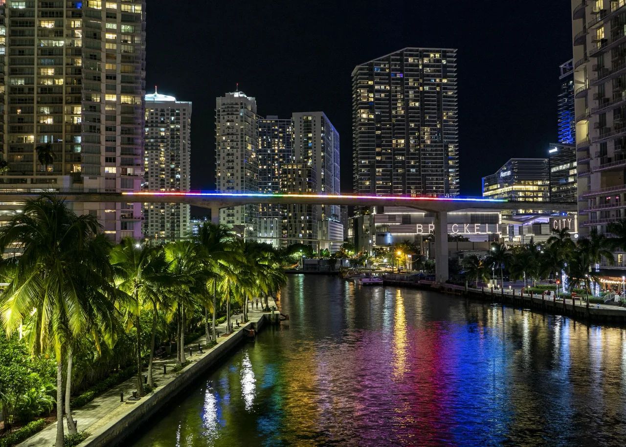 Night View of Miami River District With Lighted Metromover and Waterfront High-Rises Reflecting on the River, Showcasing the City's Vibrant Nightlife and Urban Development
