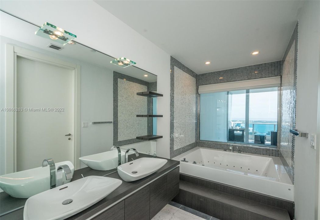 Master bathroom with upgraded bathtub and separate shower. Italian imported suspended cabinetry in dark oak finish with his and her vessel sinks in white high-gloss ceramic and lighted wall mirror, including top of the line Zuchetti faucets and fixtures.