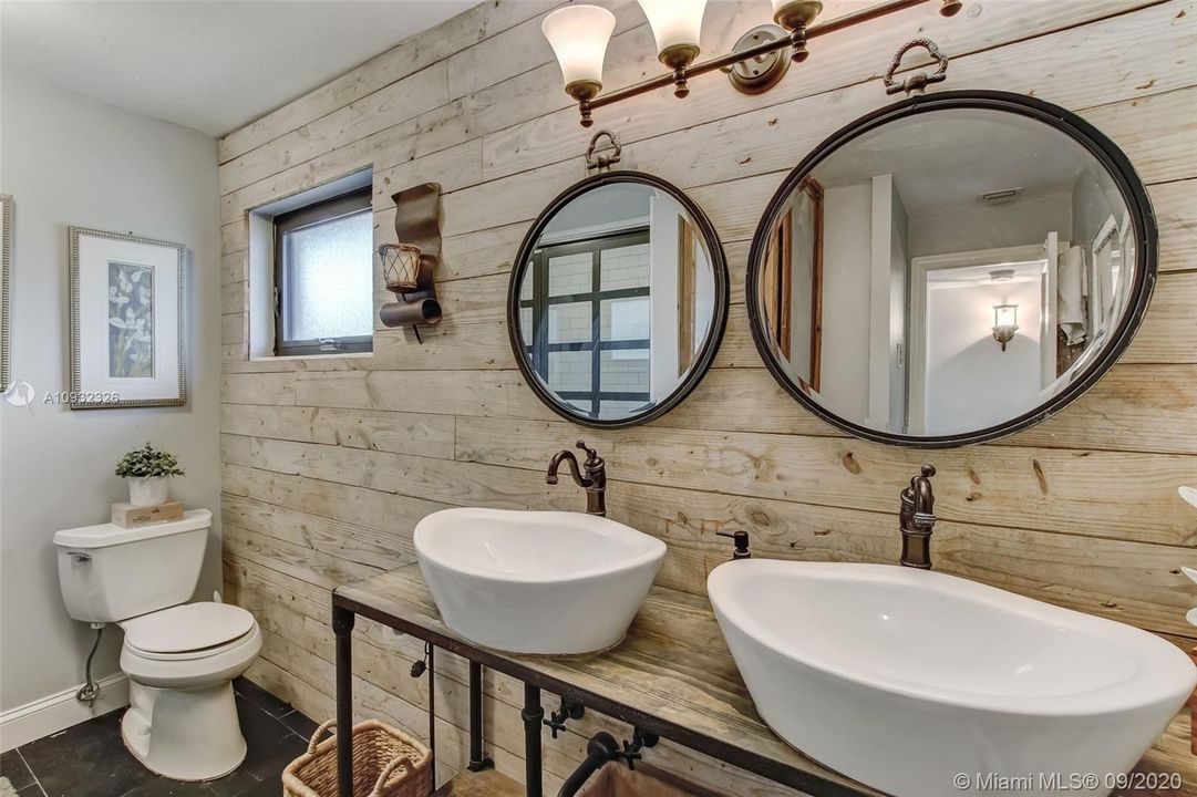 Upstairs hall bathroom remodeled in 2017 boasts custom vanity with custom plumbing fixtures; rare Dade County pine (1945) accent wall; new toilet; custom industrial themed storage cabinet and limestone tile flooring.