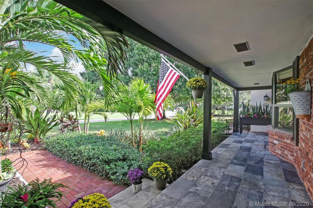 The welcoming front porch to the main house is tiled with slate and magnificently landscaped .