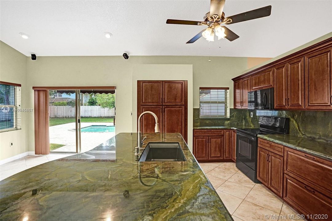 Kitchen features granite counters, pantry, black appliances, island with sink & power, wood cabinets