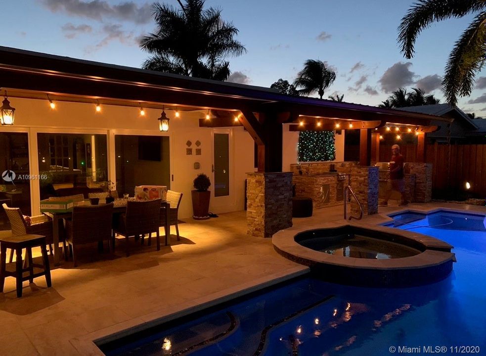 Patio in the evening, sliding doors fully open to connect Game Room with patio, following the same travertine and wood ceiling flow and providing continuity.