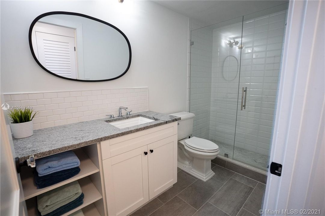 Guest bathroom showcases frameless shower brand new cabinets with granite counter top, Kohler toilet, Grohe Faucets, Porcelanosa Tiles, solidwood doors with trim combined glass doorknobs and modern baseboards.