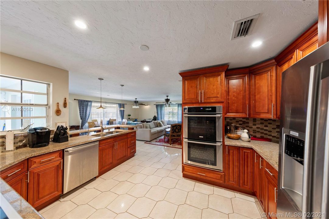CUSTOM KITCHEN W/ GRANITE COUNTER TOPS AND STAINLESS STEEL APPLIANCES OVERLOOKING FAMILY ROOM