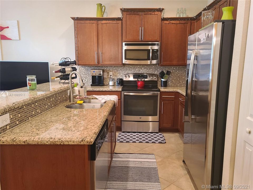 kitchen with stainless steel appliances, glass tile backsplash, granite counters, wood cabinets