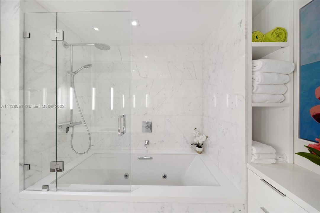Floor-to-ceiling large block Carrera Blanco marble tiles add quiet elegance to both bathrooms