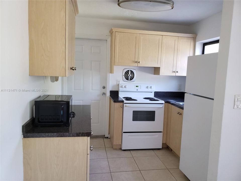 Kitchen tile floors, stove, microwave and refrigerator. Door to outside patio.