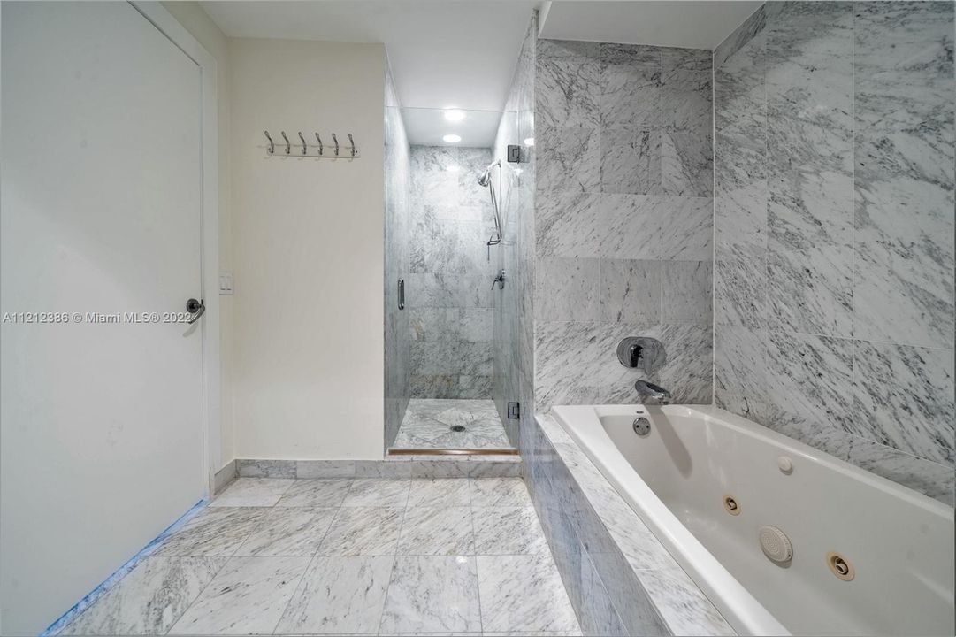 The primary bath features a marble-walled shower and a spa tub for luxurious soaking