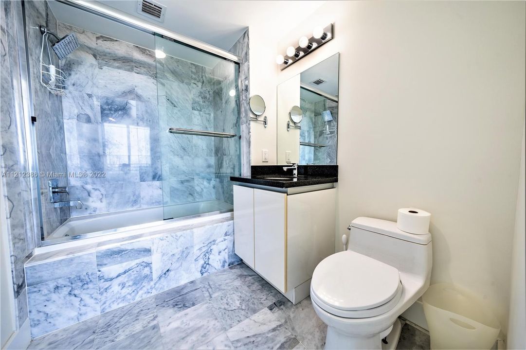The guest bath features marble-lined walls and a shower-tub