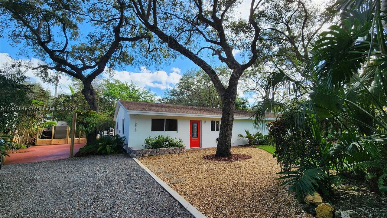 Frontal view into the home.  The grey gravel and red cement pavement is parking area.