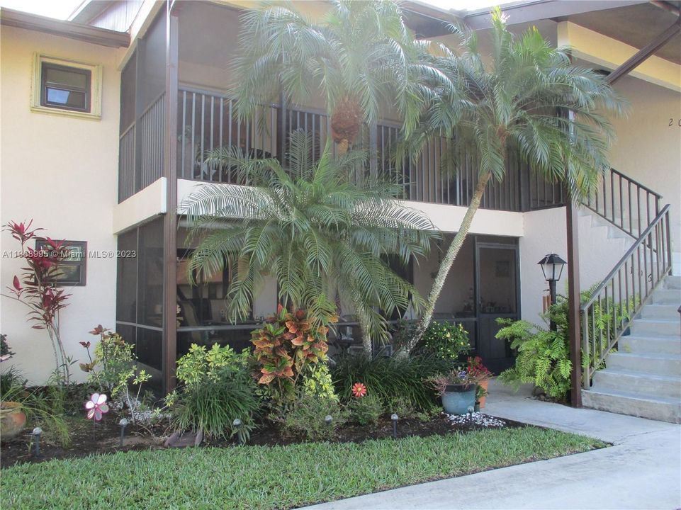 VIEWING THE ENTRANCE INTO THE CONDO WITH PALM TREES AND A GARDEN AREA.