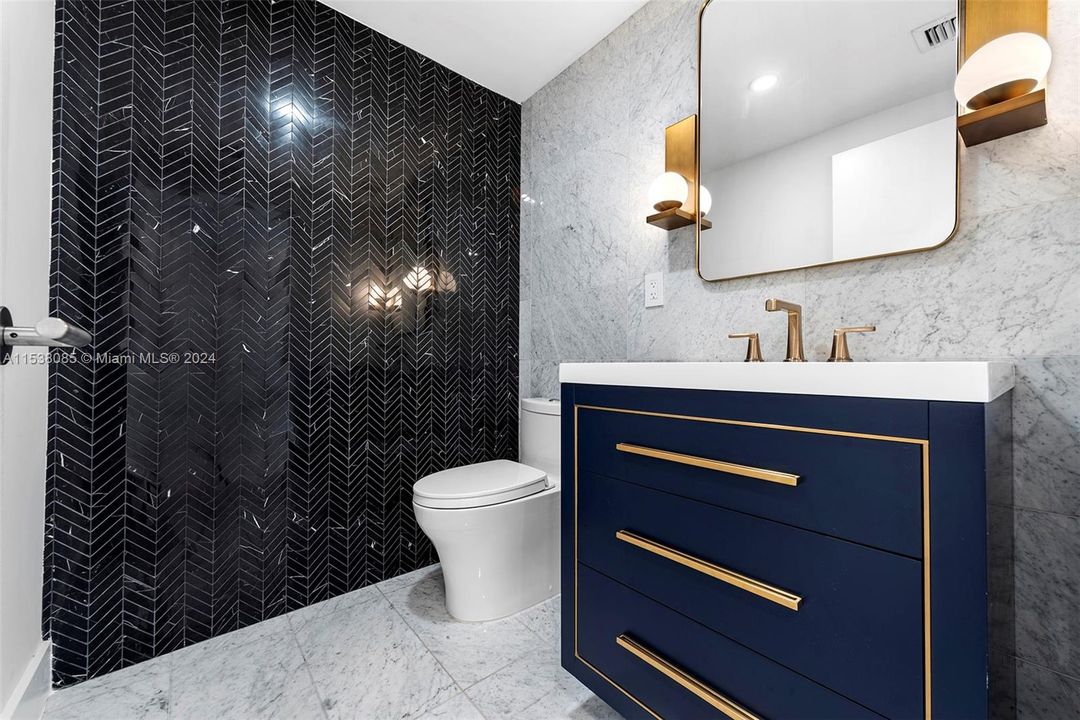 Powder room featuring Nero Marquina chevron mosaic marble wall, floating Madeli vanity with brass sconce lighting, mirror, and Brizo brass fixtures. Toto dual flush toilet