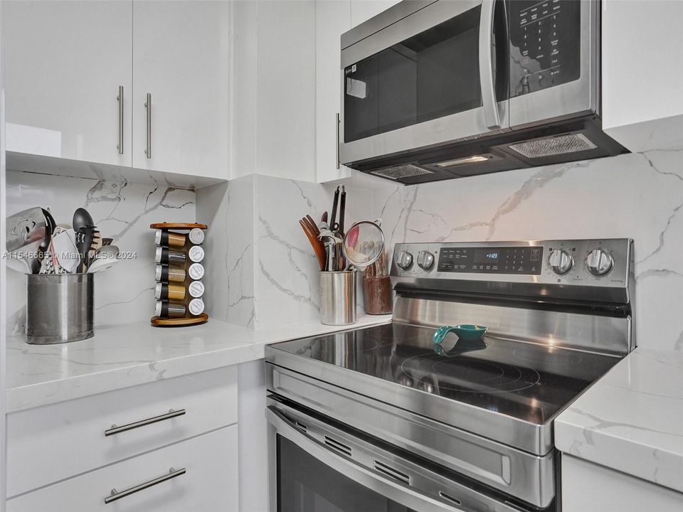 FULLY RENOVATED EAT-IN KITCHEN WITH WHITE CABINETS, QUARTZ COUNTERTOPS AND BACKSPLASHES, STAINLESS STEEL APPLIANCES, TOP-OF-THE-LINE CERAMIC FLOORS, BREAKFAST AREA, SLIDING GLASS DOORS AND LAKE VIEWS