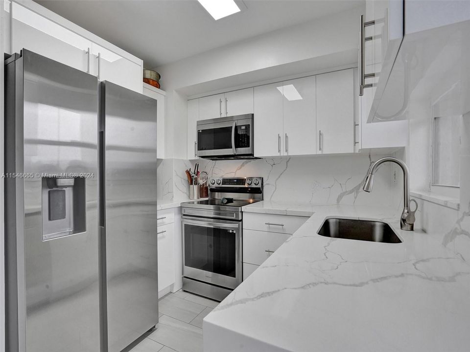 FULLY RENOVATED EAT-IN KITCHEN WITH WHITE CABINETS, QUARTZ COUNTERTOPS AND BACKSPLASHES, STAINLESS STEEL APPLIANCES, TOP-OF-THE-LINE CERAMIC FLOORS AND LAKE VIEWS
