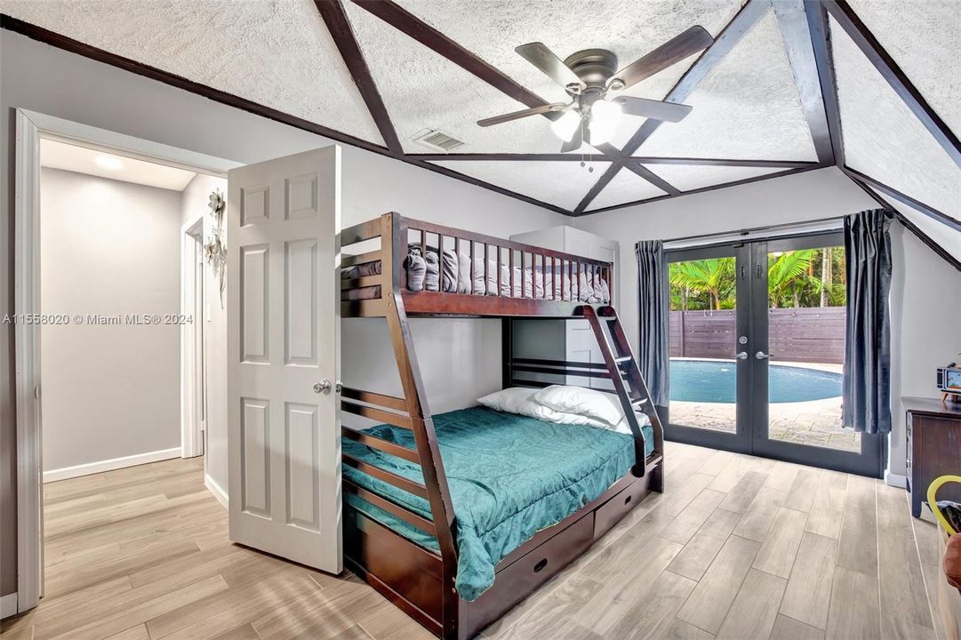 2nd bedroom downstairs (this one w/ beamed ceiling detail) which leads right to pool deck. Plank tile flooring runs into the room. No built in closet, but closet cabinet can convey to buyer.