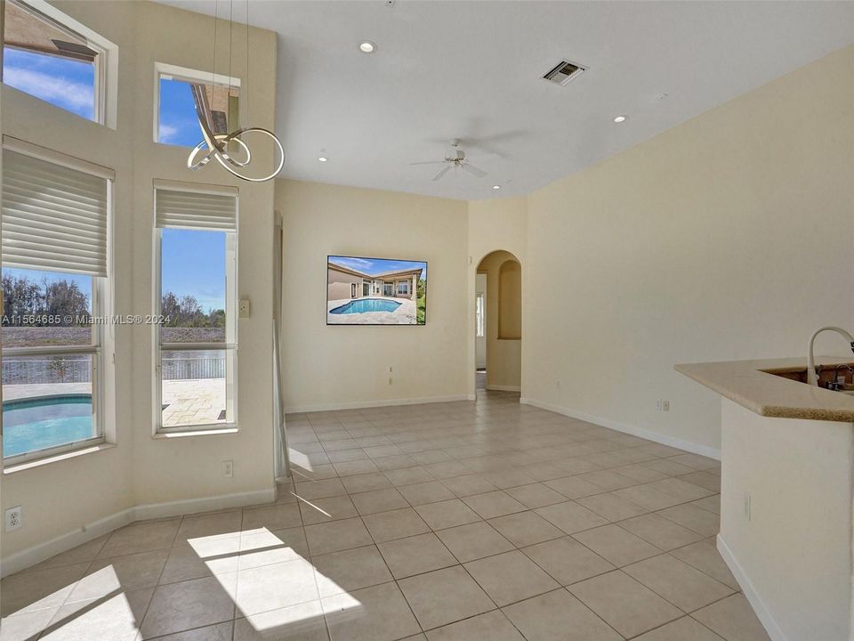 Open concept kitchen and living area shares a casual dining area by the windows near pool