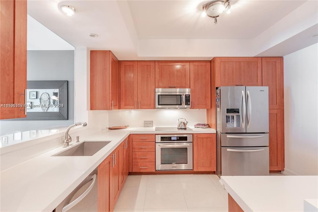 Open concept kitchen equipped with stainless steel appliances, wood cabinetry and sleek modern countertops and backsplash.