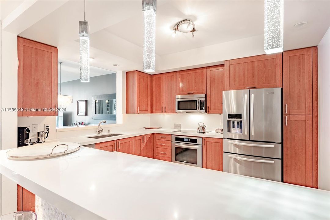 Open concept kitchen equipped with stainless steel appliances, wood cabinetry and sleek modern countertops and backsplash.