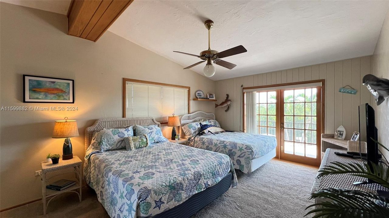 This bright and airy guest bedroom features plush carpeting, twin beds with coastal-themed bedding, and ample closet space. French doors lead to a balcony, inviting in the ocean breeze.