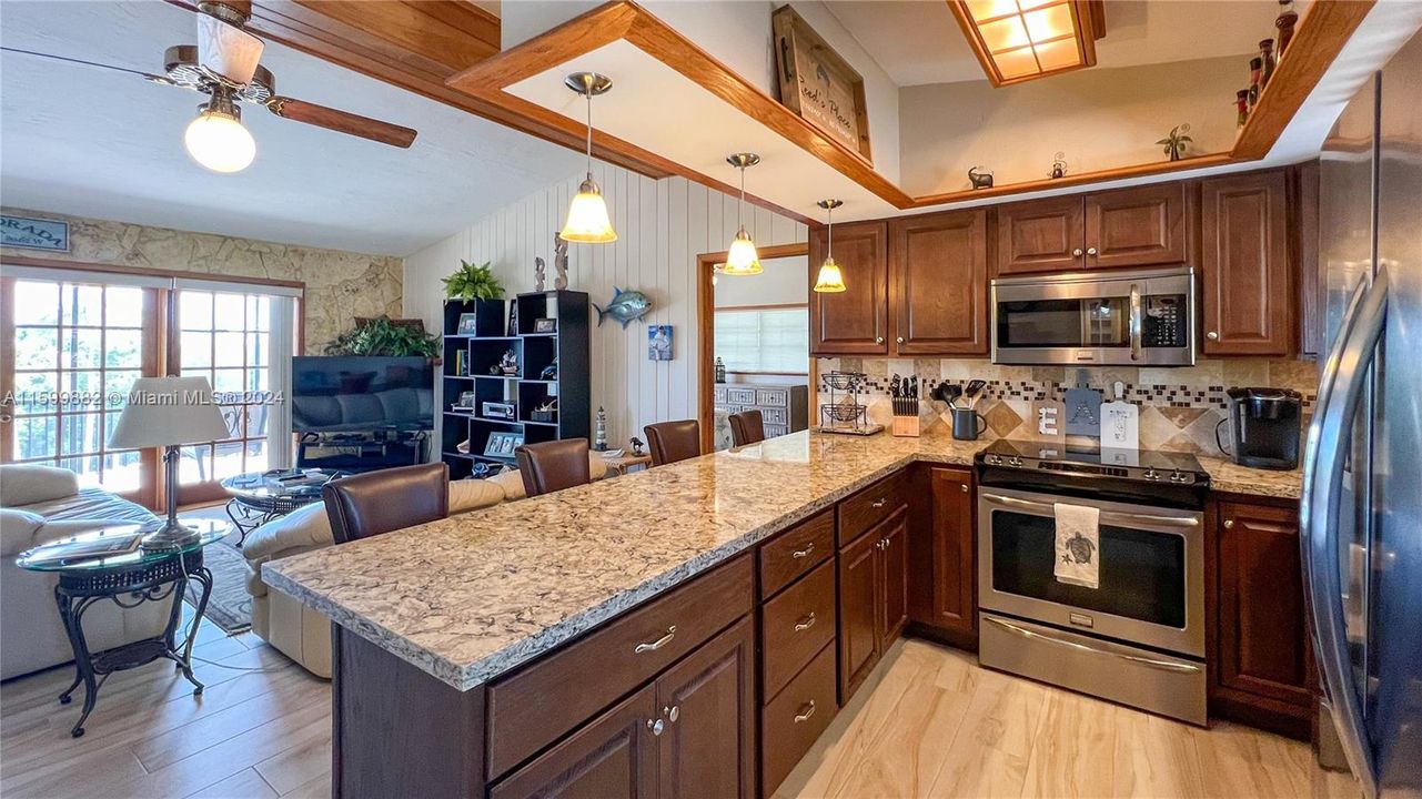 This well-equipped kitchen boasts modern stainless steel appliances, rich wooden cabinetry, and elegant granite countertops. The overhead lighting and breakfast bar provide both functionality and a warm ambiance for casual dining.