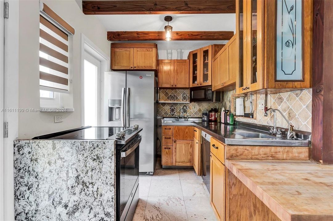 Custom Designed kitchen chef's kitchen with wood cabinetry, stone accents and stainless steel refrigerator/freezer. Also features stainless countertops and two sinks. There is a butcher-block table height extension.