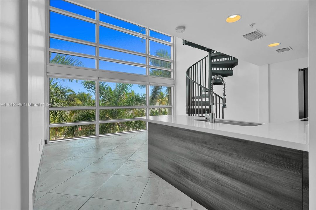 Double-height ceiling loft with modern kitchen, stainless steel appliances, spiral staircase, and mezzanine level. Bright, airy, and perfect for relaxation or entertainment.