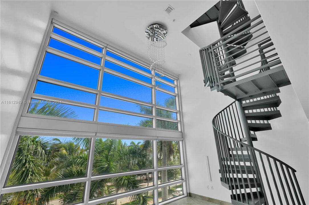 Double-height ceiling loft with modern kitchen, stainless steel appliances, spiral staircase, and mezzanine level. Bright, airy, and perfect for relaxation or entertainment.