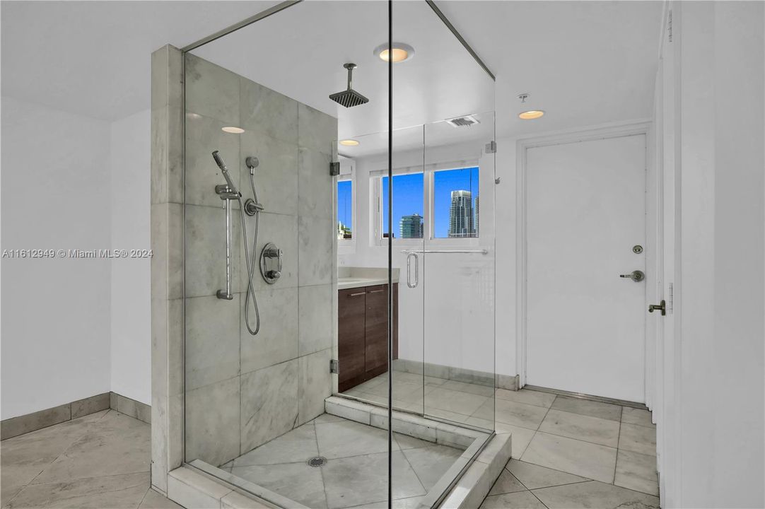 Modern master bath with a glass-enclosed shower, marble tiles, and city views. Sleek and luxurious design for a spa-like experience.