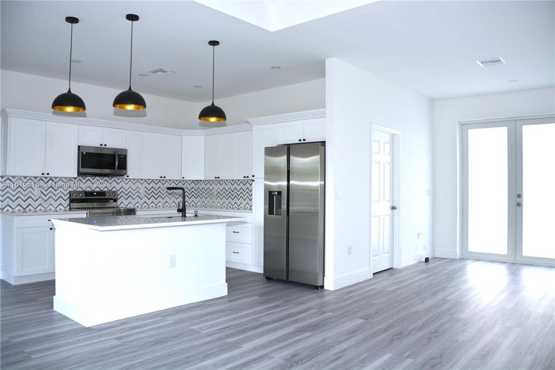 Kitchen with appliances with stainless steel finishes, white cabinets, a kitchen island with sink, backsplash, and water prove laminated floor