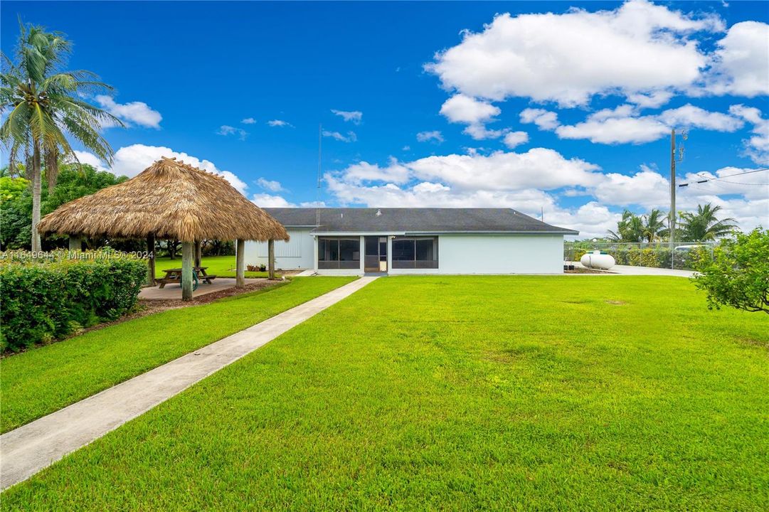 BACK VIEW OF THE HOUSE WITH  COVERED SCREEN PATIO, UNSEEN IS INTERIOR STORAGE ROOM..CONCRETE WALKWAY LEADS TO THE TIKI HUT AND WAREHOUSE. PROPANE FOR GNERATOR PHOTOS OF WAREHOUSE TO FOLLOW