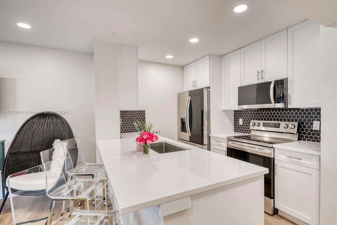 Open, renovated kitchen with high quality white shaker cabinets, quartz counters, stainless appliances and counter seating.