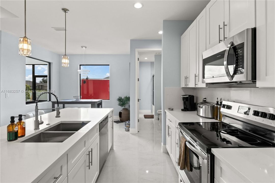 Kitchen featuring white cabinets, hanging light fixtures, sink, stainless steel appliances, and light stone countertops