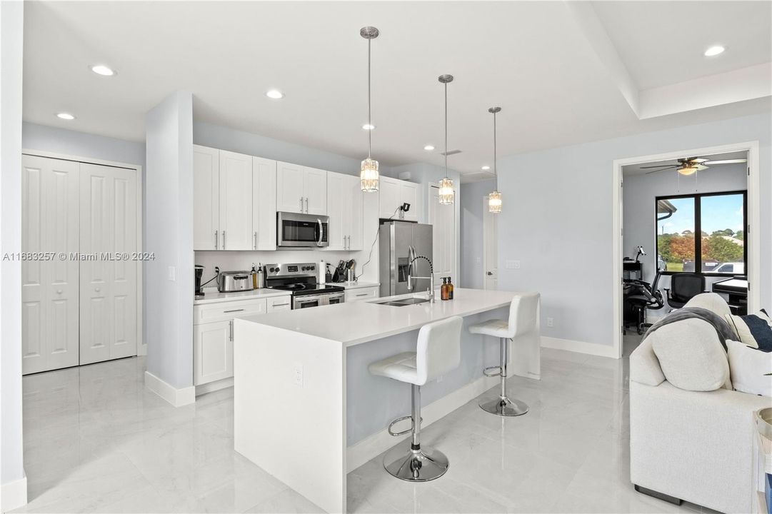 Kitchen with ceiling fan, hanging light fixtures, white cabinets, appliances with stainless steel finishes, and an island with sink