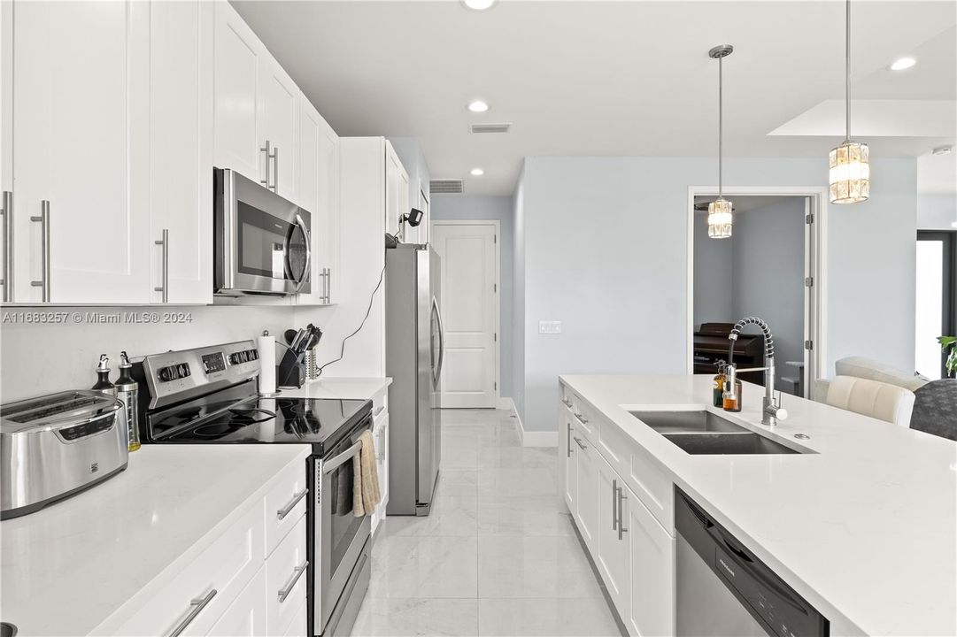 Kitchen featuring appliances with stainless steel finishes, decorative light fixtures, sink, and white cabinets