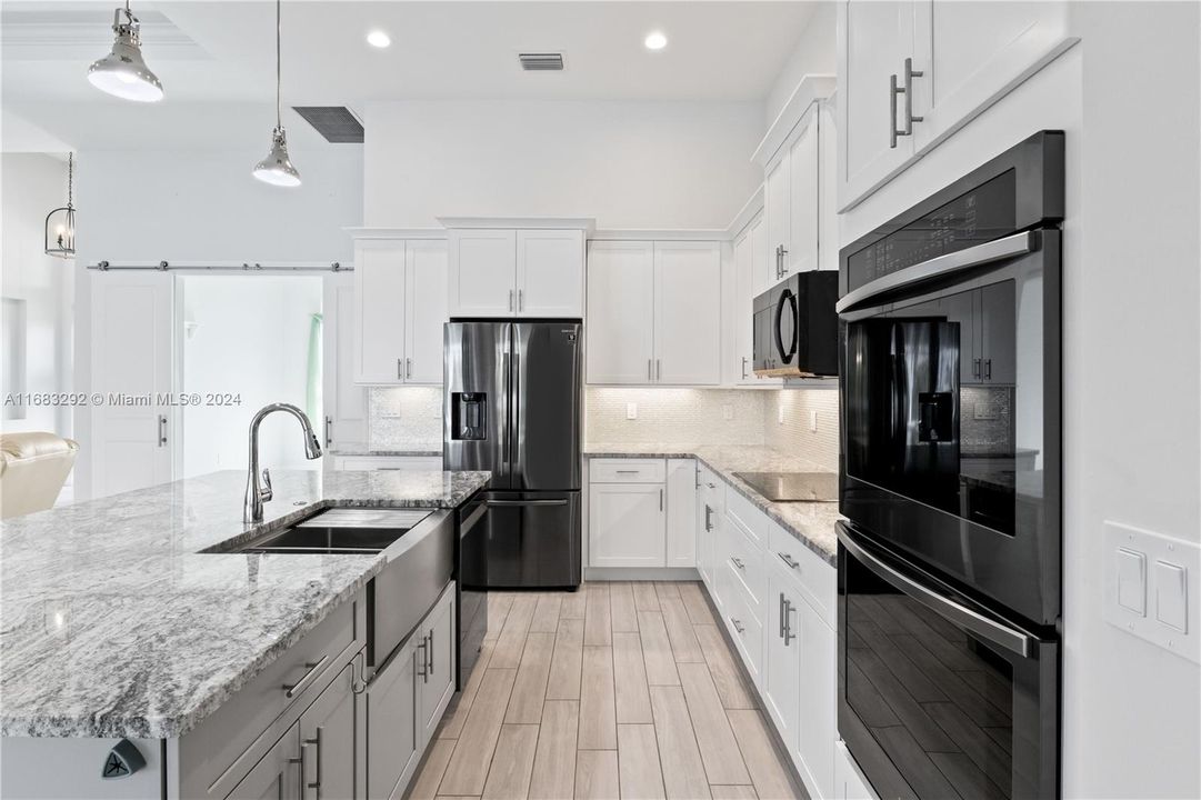 Kitchen with decorative light fixtures, black appliances, decorative backsplash, white cabinets, and sink