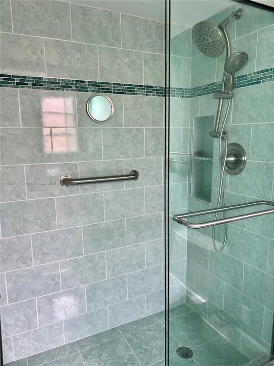 Updated primary walk-in shower featuring beautiful tile work, glass tile border and grab bar.