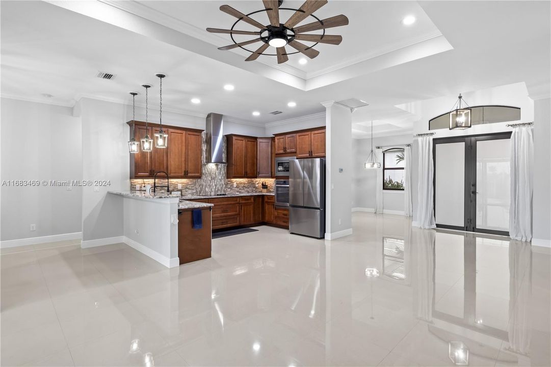 Kitchen featuring appliances with stainless steel finishes, tasteful backsplash, wall chimney range hood, a tray ceiling, and ceiling fan