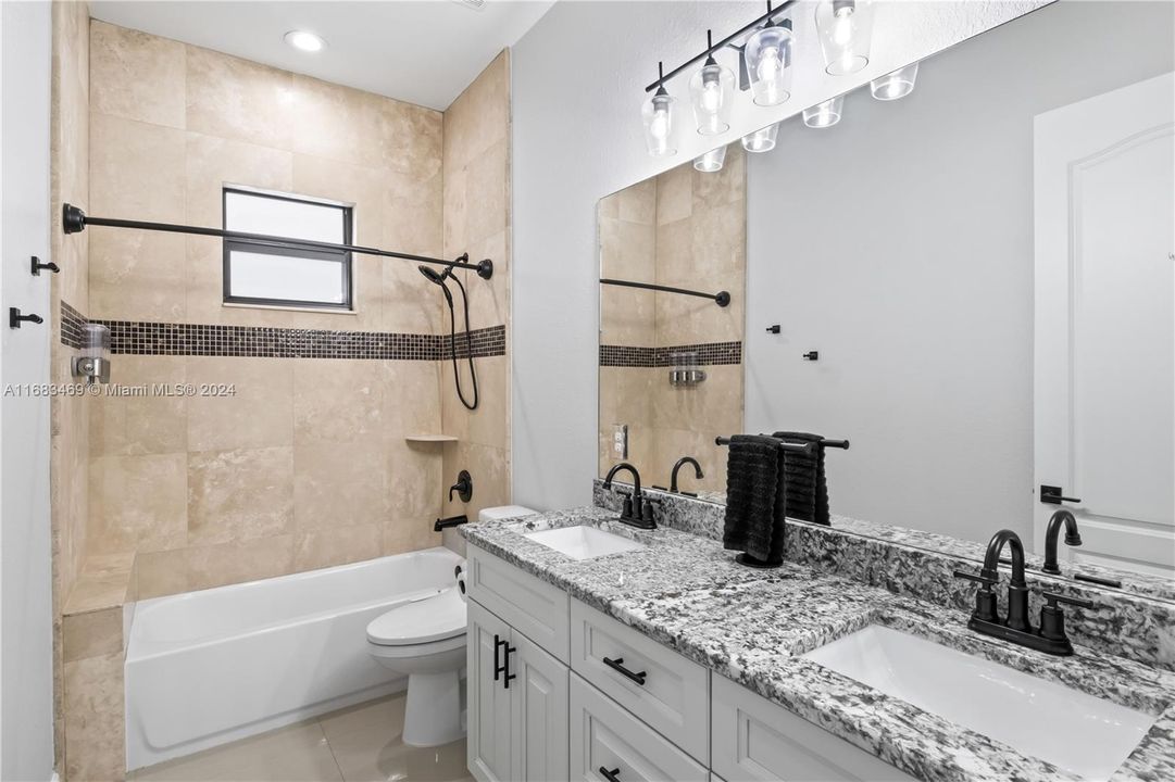 Full bathroom with tiled shower / bath combo, toilet, tile patterned floors, and vanity