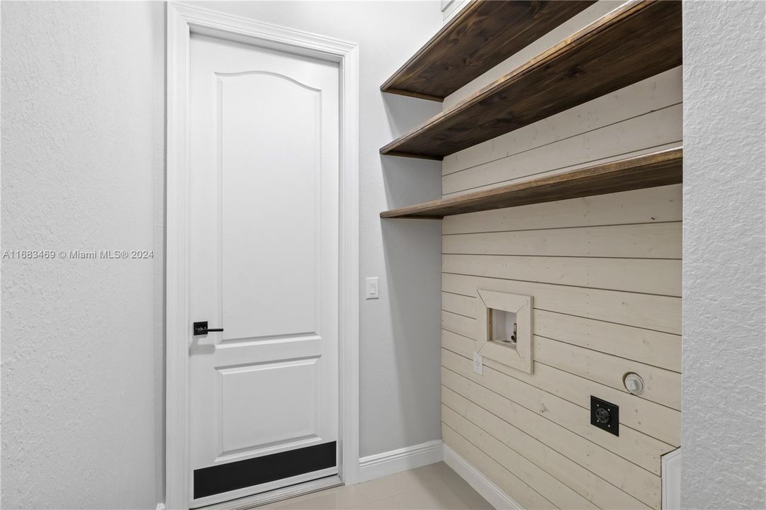 Laundry room is located inside the home and is accented by beautiful shiplap walls and shelving.