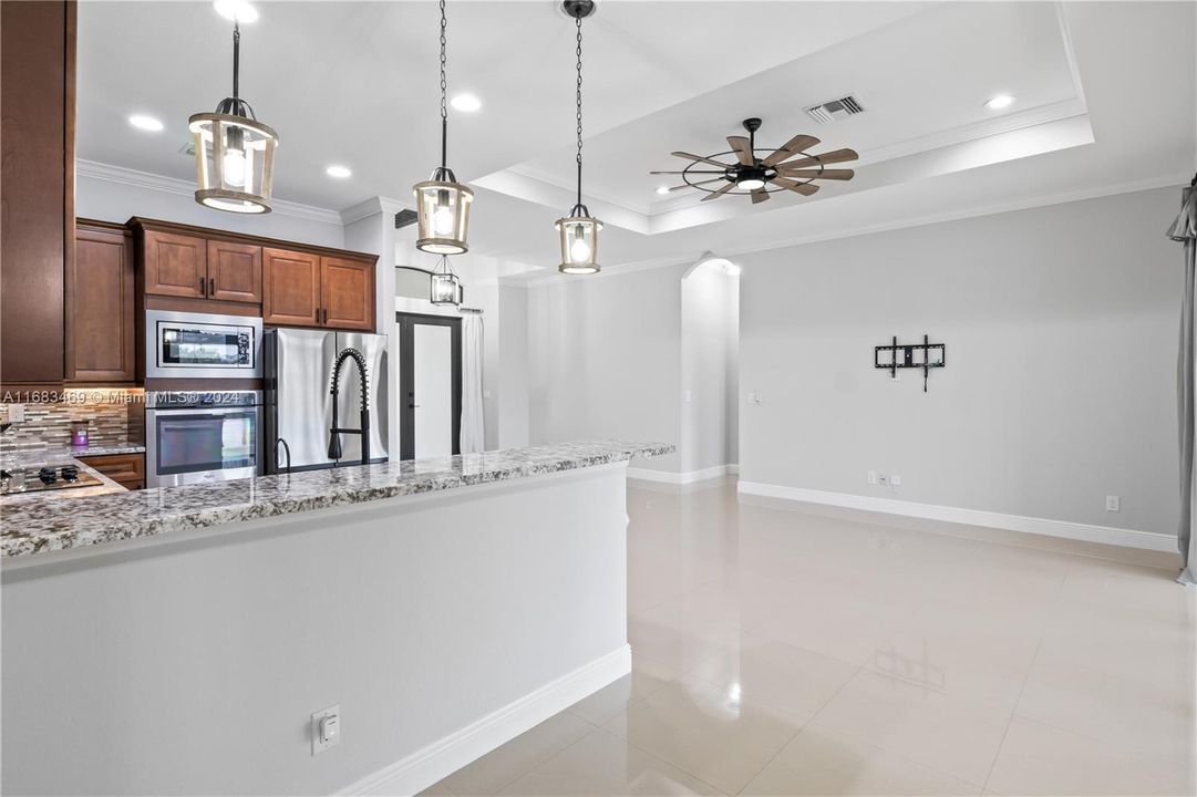 Kitchen featuring ceiling fan, hanging light fixtures, light stone counters, light tile patterned flooring, and stainless steel appliances