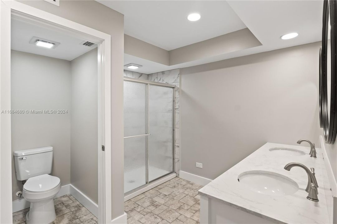 Secondary mater bathroom featuring a shower with shower door, tile patterned flooring, toilet, and dual bowl vanity