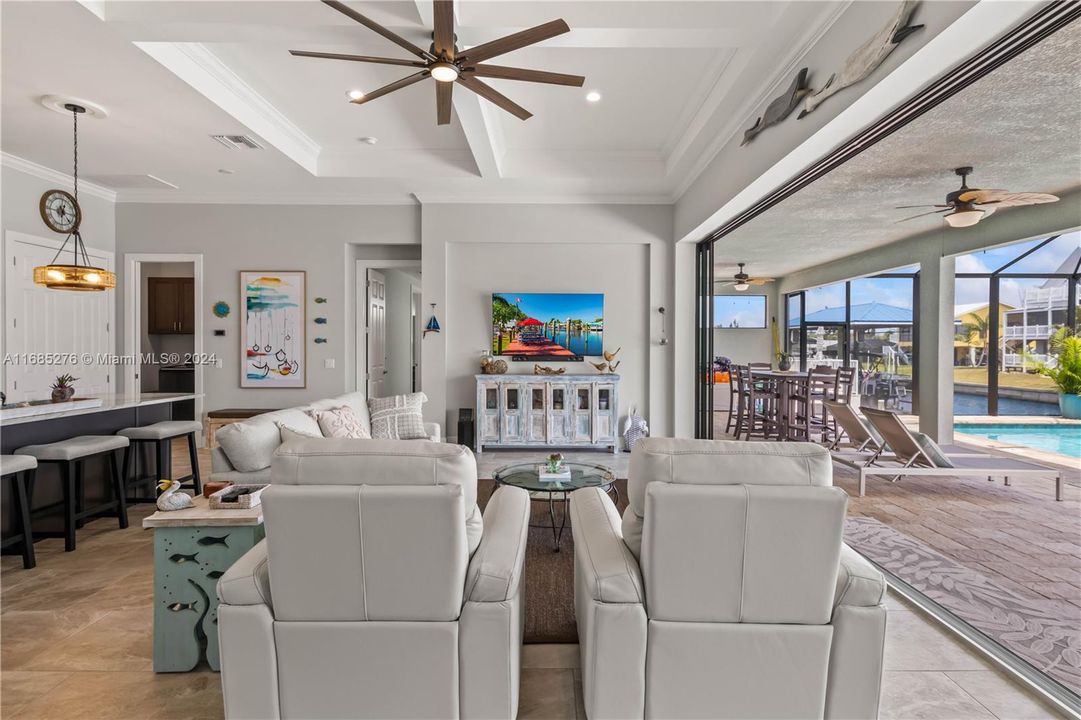 Massive living room featuring a coffered ceiling, all tile floors, accent wall and four hurricane impact sliders that disappear and blend the inside and outside living area seamlessly!