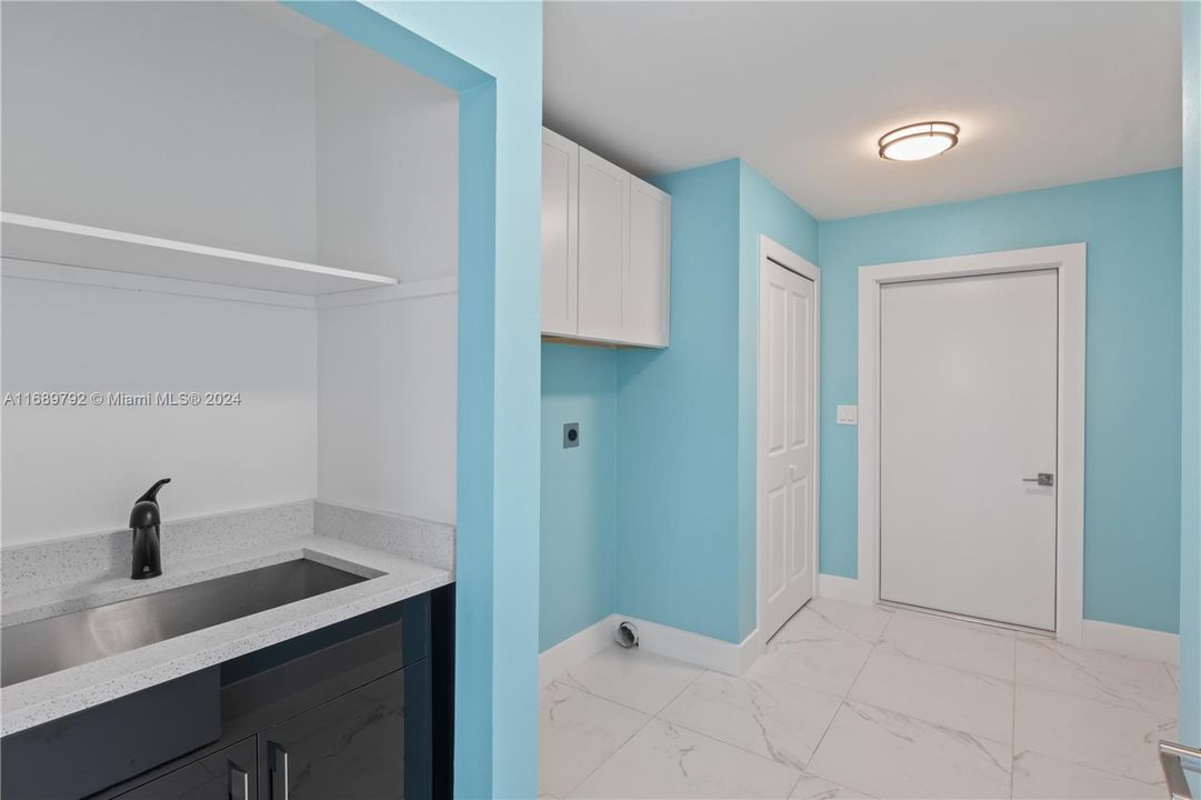 Washroom with light tile patterned floors, sink, electric dryer hookup, and cabinets