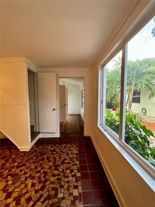 The picture shows a corridor that leads outside the living room, featuring a large window on the right and staircase access on the left to the second floor, where the 250 sq. ft. master bedroom is located. The corridor connects to the front door and includes two additional doors leading to the bathroom and a smaller bedroom.