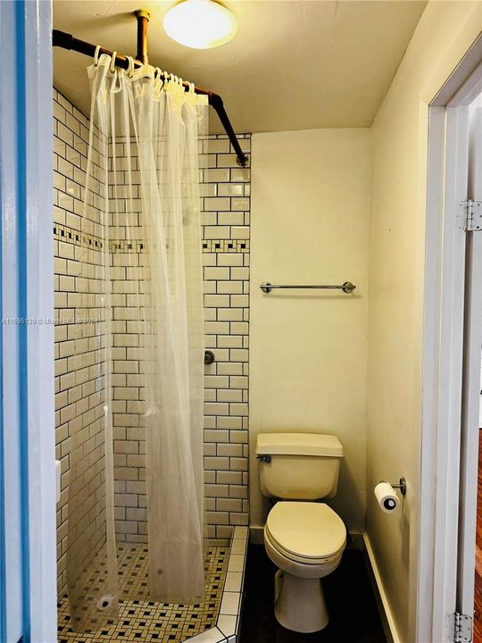 The bathroom, accessible through two separate doors from the ground-level bedroom and the corridor, features a corner shower with white subway tiles and mosaic accents, a sleek black vanity with a square sink and mirror, white-painted walls, and dark flooring, creating a compact, modern, and functional design.