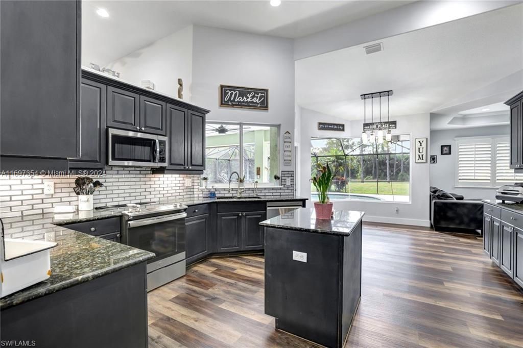 Kitchen featuring appliances with stainless steel finishes, dark stone counters, dark hardwood / wood-style floors, sink, and a center island