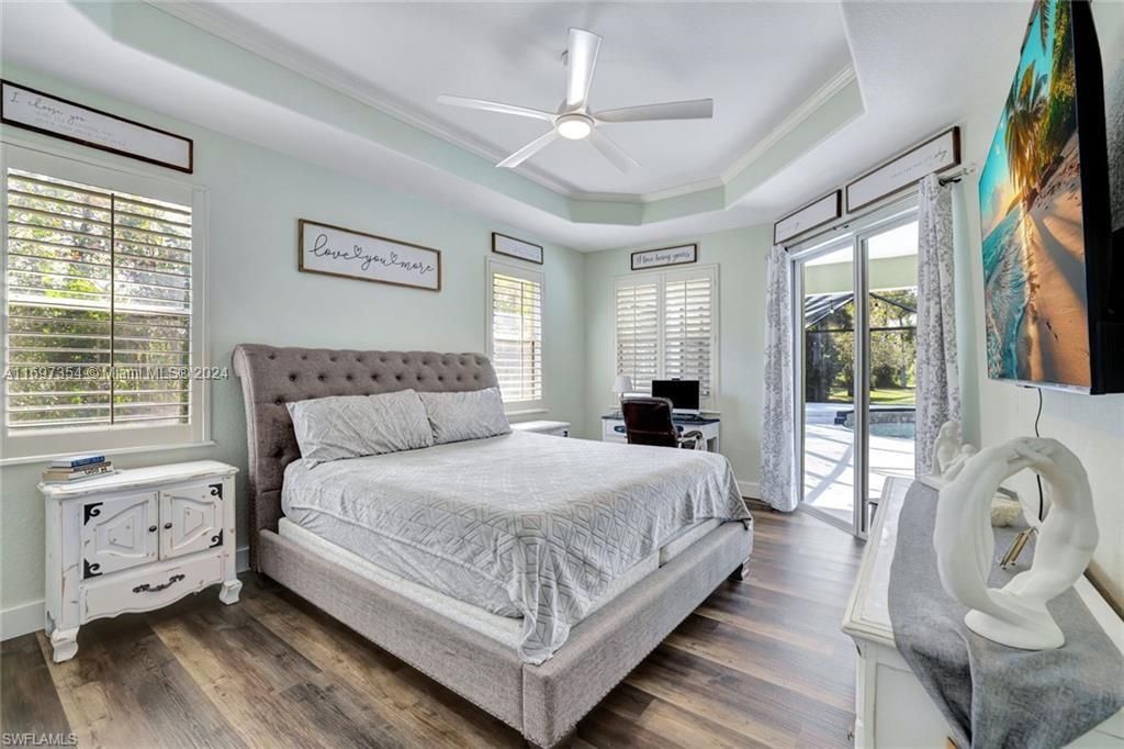 Bedroom featuring dark wood-type flooring, ceiling fan, multiple windows, and a raised ceiling