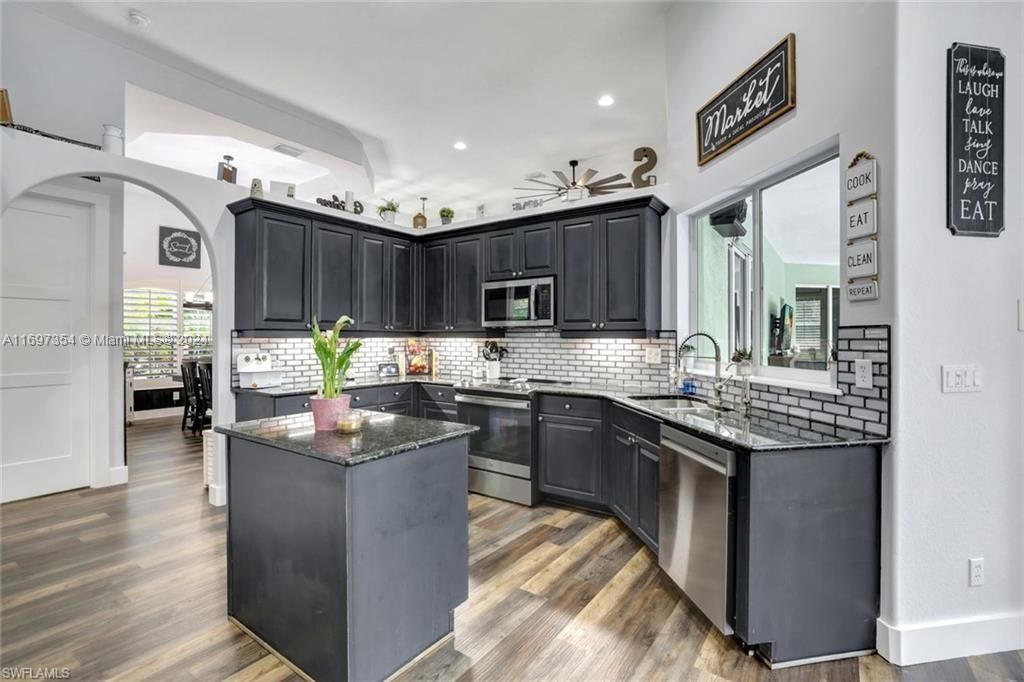 Kitchen with appliances with stainless steel finishes, sink, dark stone counters, and dark hardwood / wood-style flooring