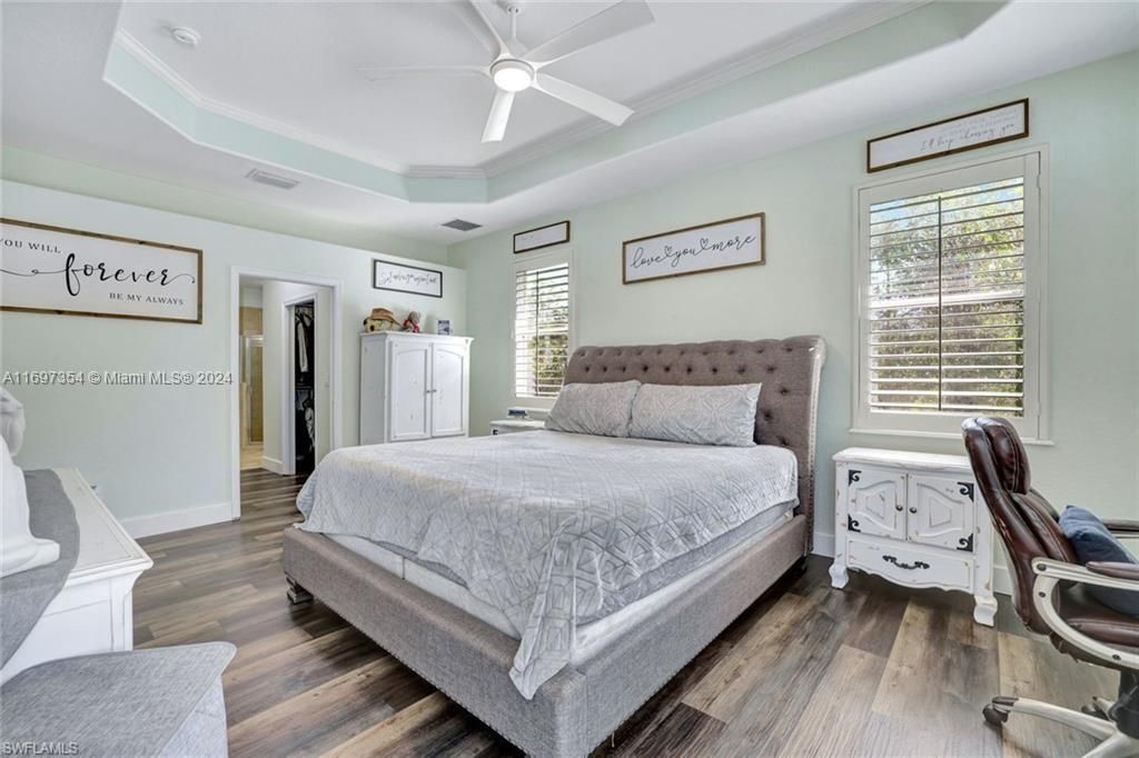 Bedroom featuring dark wood-type flooring, ceiling fan, multiple windows, and a raised ceiling