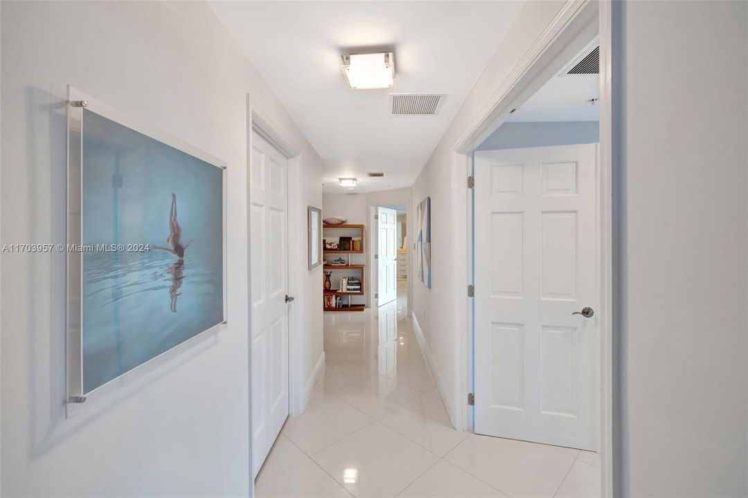 Hallway from living area to bedrooms. Powder room on the left, primary suite on the right (double door entry), laundry room down on the left, and guest bedroom suite at end of hallway ahead on right